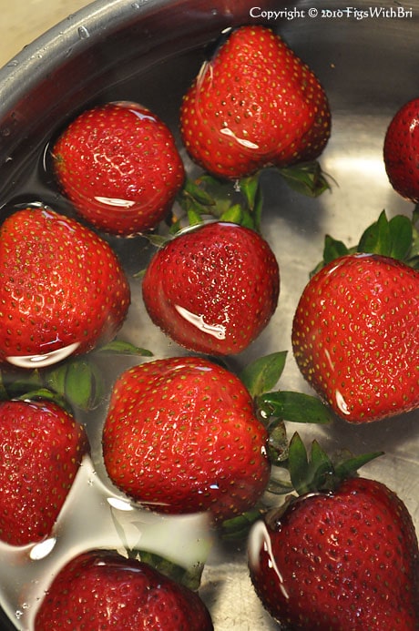 Organic strawberries floating in bowl of water