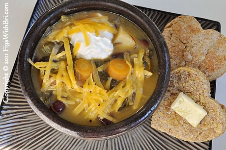 bowl of vegetable soup topped with yogurt, grated cheese, with buttered biscuits